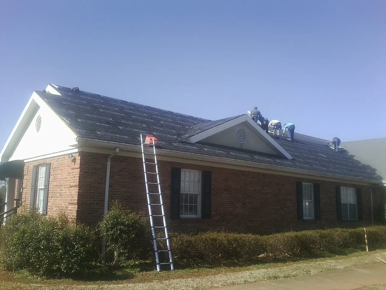 Crew tearing shingles off a brick ranch roof with a ladder set — Emergency Roof Repair work by our crew in Kingsburg