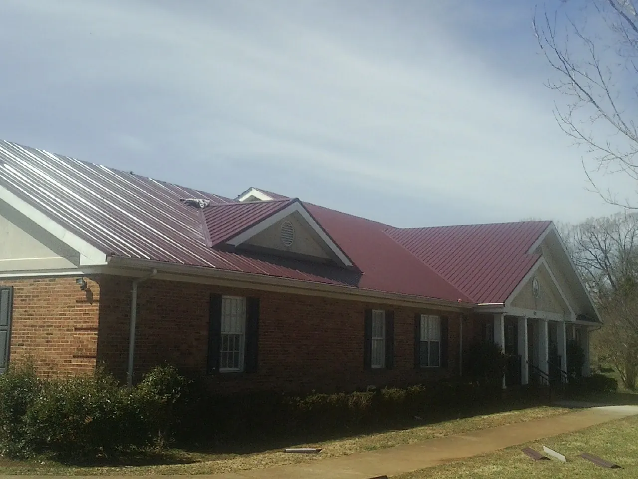 Red metal roof with gabled entries on a long brick building, from a Hail Damage Roof Repair job in Kingsburg