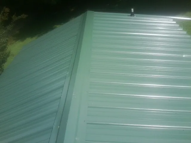 New green metal panels meeting at the ridge of a roof — Flat Roof Repair work by our crew in Kingsburg