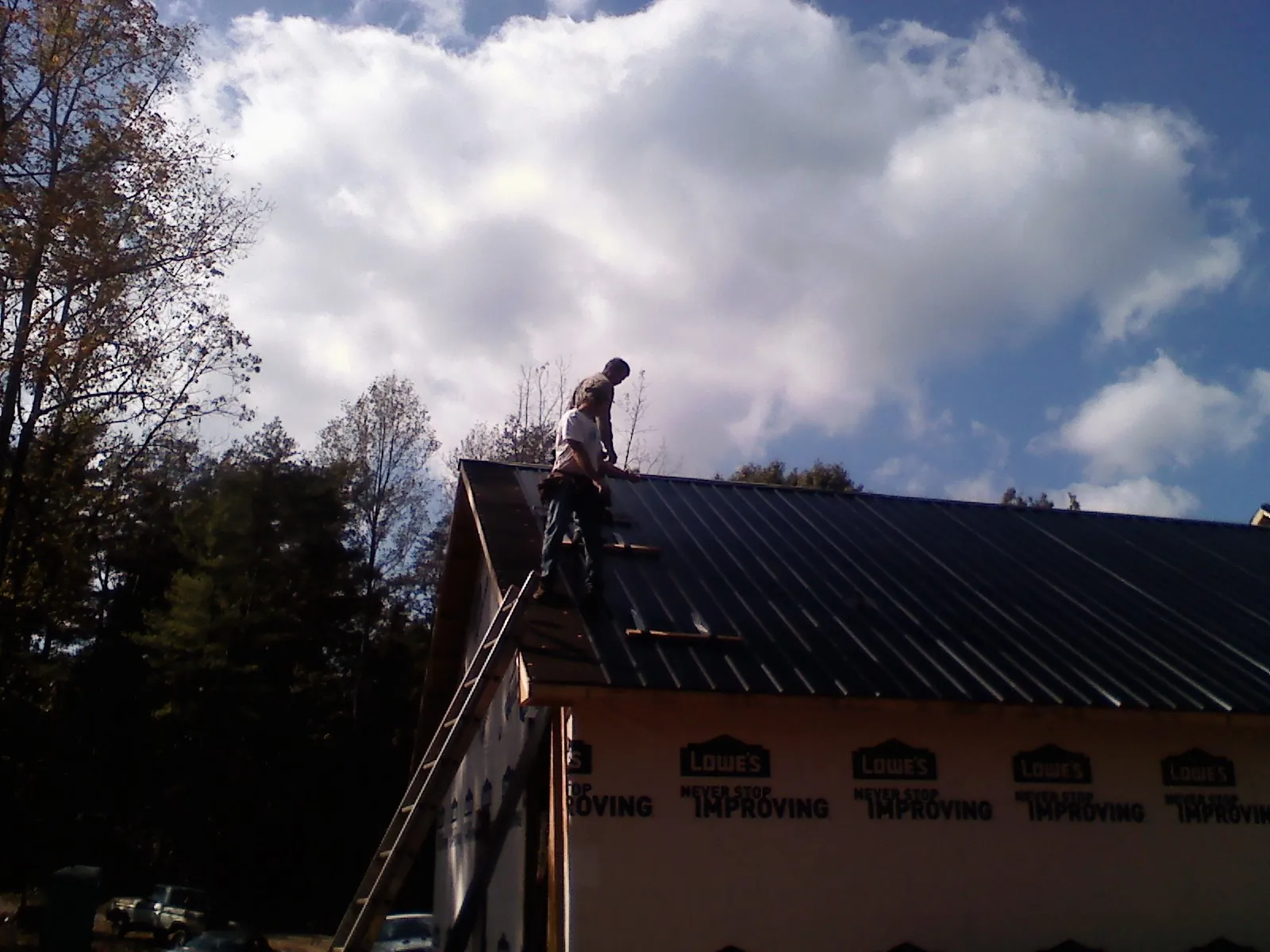 Roofer fastening dark metal panels high against a cloudy sky, from a Roof Inspection job in Kingsburg