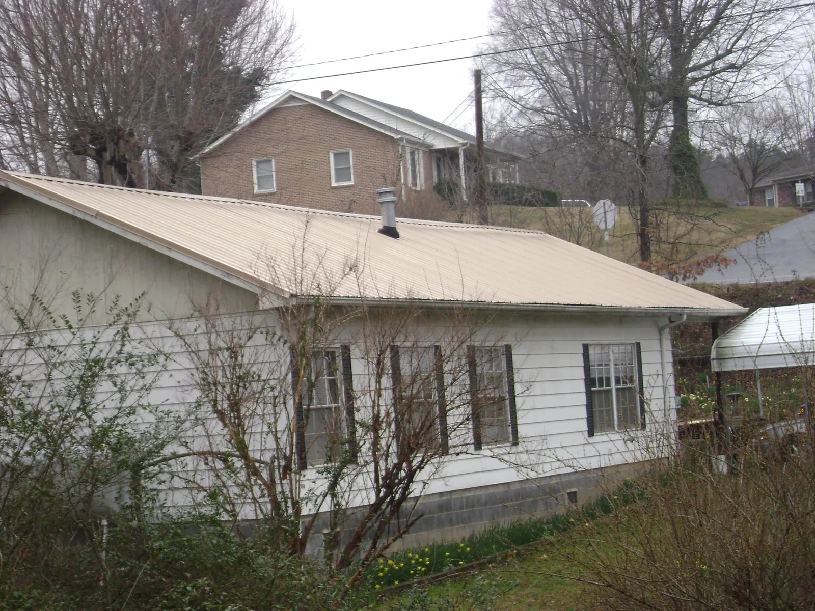 Tan metal roof on a white sided house set into a hillside — Commercial Roofing by Roofing Brothers in Kingsburg